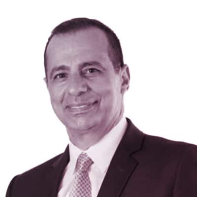 Man in a suit and tie smiling, facing forward, with a plain light background.