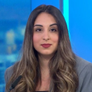 A woman with long brown hair and a gray blazer sits in a studio setting with blue lighting in the background, ready to discuss the highlights of CyberWeek 2024.